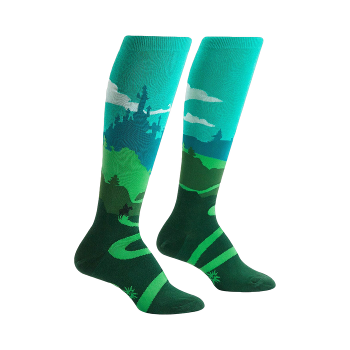 Pair of teal and green knee-high socks depicting a whimsical landscape with a castle, winding road, and a moose. }}