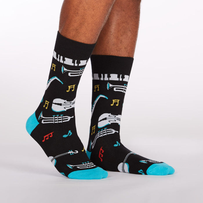 A pair of black socks with a pattern of musical instruments and notes. The socks have blue heels and toes.