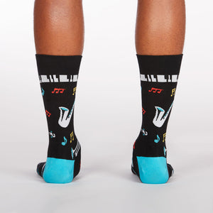 A pair of black socks with a pattern of musical instruments and notes. The socks have blue heels and toes.