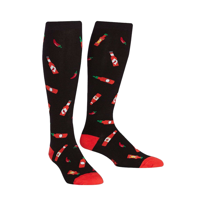 Pair of black knee-high socks with a pattern of red hot sauce bottles and chili peppers.  The socks have red cuffs. }}