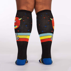 A pair of black knee-high socks with a colorful pattern of monsters and rainbows. The socks have a blue toe and heel, and a red, yellow, and blue striped top. The socks are shown on a plus-size model.