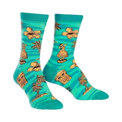 Crew socks in teal, adorned with orange hibiscus flowers, hula dancers, tiki masks, and palm trees. A fun, tropical design.