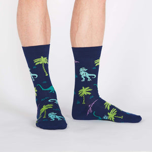 A pair of blue socks with a pattern of dinosaurs and palm trees.