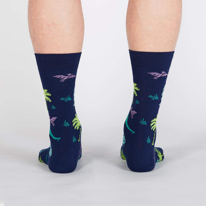 A pair of blue socks with a pattern of dinosaurs and palm trees.