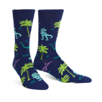 Pair of navy blue crew socks featuring a fun pattern of green and purple dinosaurs and palm trees.