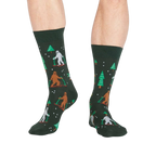 Lifestyle shot showing the 'Ready, Yeti, Go!' socks on a person's legs.  The socks are dark green with a festive pattern.
