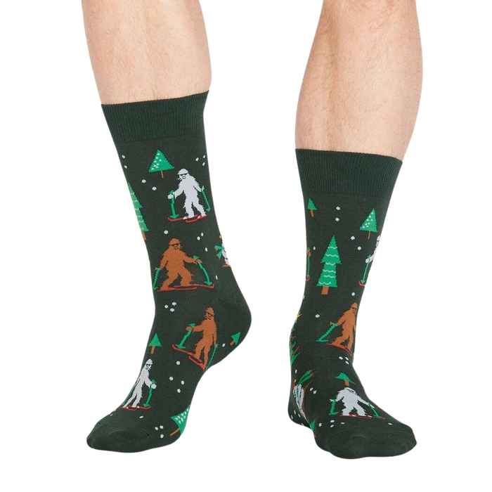 A pair of green socks with a pattern of Bigfoot and a bear skiing down a mountain on them.