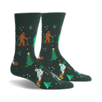 A pair of dark green crew socks with a whimsical Christmas design. Features Bigfoot characters skiing, snowmen, and Christmas trees.