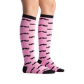 Lifestyle shot showing the Mustache knee-high socks on a person's legs. Pink and black pattern.