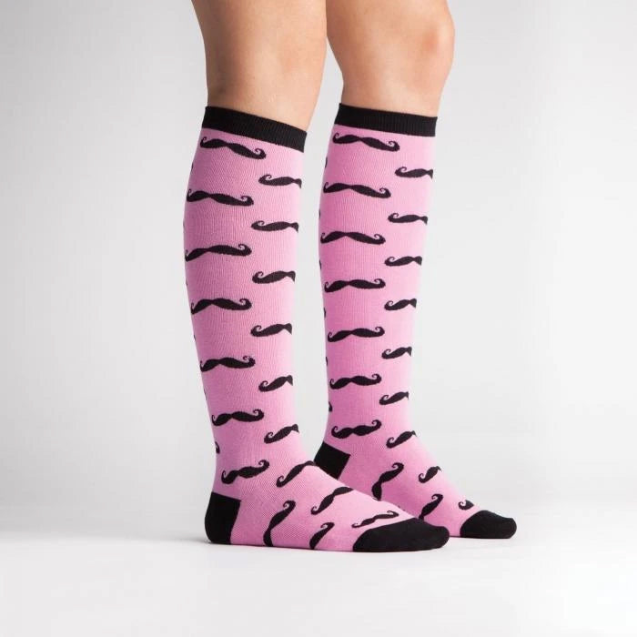 A pair of pink knee-high socks with a pattern of black mustaches.