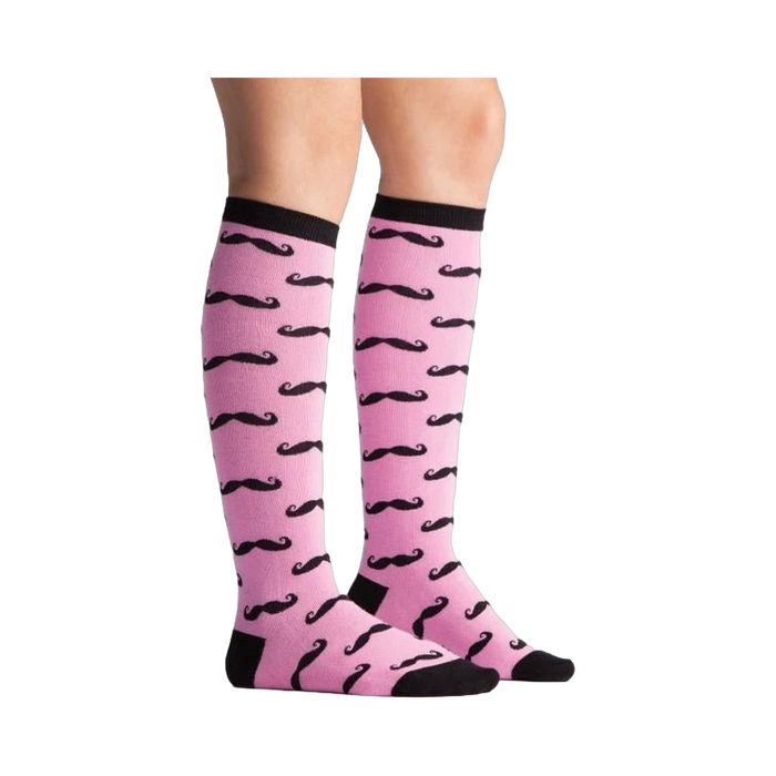 Lifestyle shot showing the Mustache knee-high socks on a person's legs. Pink and black pattern.