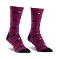 A pair of purple crew socks with a fun pattern. Black mustaches and multicolored hearts are playfully scattered across the socks, which have black heels and toes.