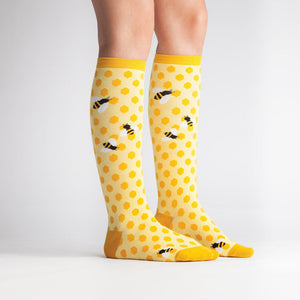 Yellow knee-high socks with a honeycomb pattern and bumblebees on them.