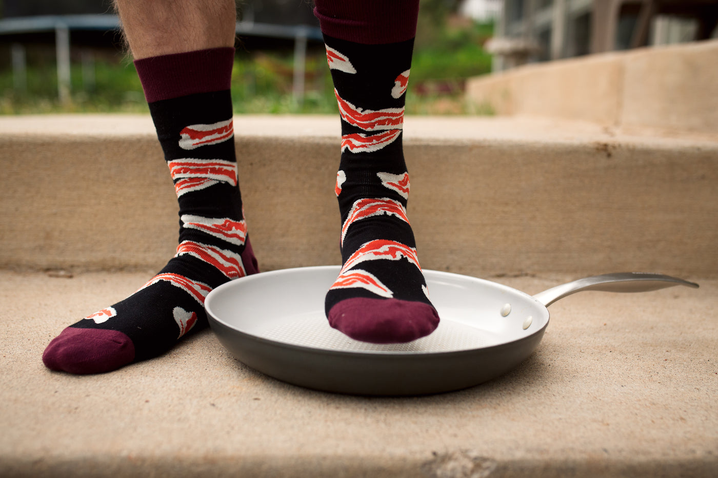 [lf] Person wearing black and red bacon-patterned socks stands with one foot in a frying pan.