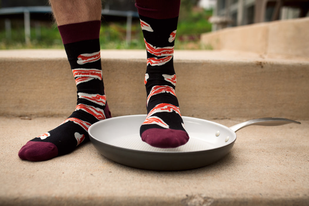 A pair of black socks with a pattern of bacon strips. The socks have a maroon toe, heel, and cuff.