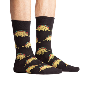 Lifestyle photo showing Tacosaurus socks on a person's feet. The socks are black with a fun taco-dinosaur pattern.