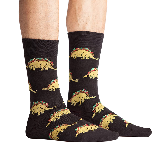 Lifestyle photo showing Tacosaurus socks on a person's feet. The socks are black with a fun taco-dinosaur pattern.