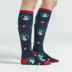 A pair of knee-high socks with an allover pattern of cartoon owls wearing glasses. The socks are dark blue with red cuffs and green toes and heels.