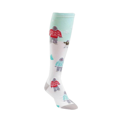 Knee-high socks in white with a teal background. The design features Yetis in red and teal sweaters, a small dog, and tiny trees.