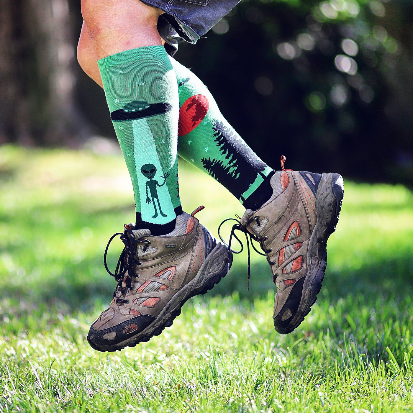 [lf] Person in hiking boots and alien-themed socks stands on grass, mid-stride.