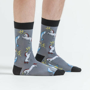 A pair of gray socks with a pattern of cartoon narwhals and unicorns fighting each other. The socks have black toes and heels.