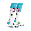 A pair of white knee-high socks with a playful design.  Blue accents at the top and bottom. Penguins skiing in neon pink, green, and black are featured on a white background with light blue snowflake accents at the top.