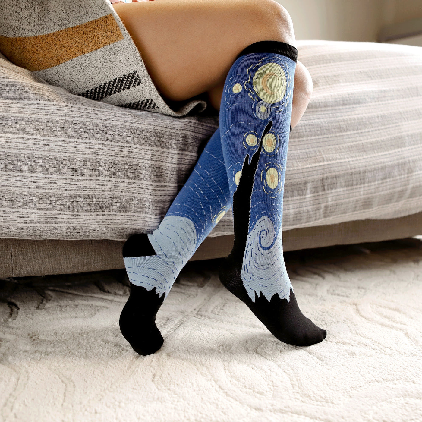 [lf] Person relaxing on a bed, wearing blue "Starry Night" patterned socks with black toes and heels.