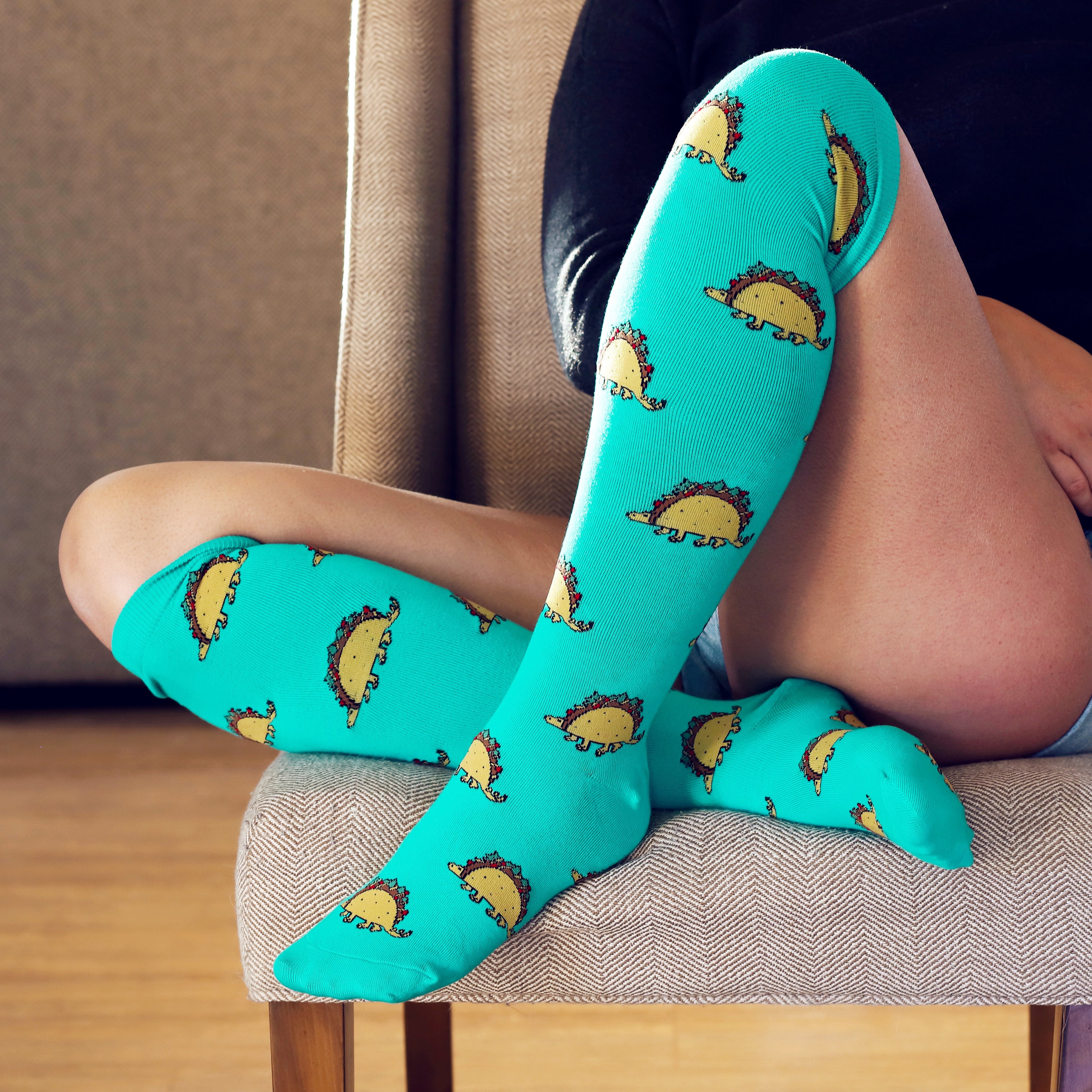 [lf] Person seated, wearing teal knee-high socks with cute taco dinosaur patterns.