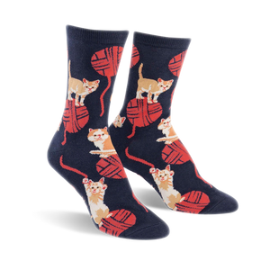A pair of crew socks in navy blue with a playful pattern of orange kittens batting at red yarn balls.