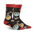 A pair of black crew socks with a space theme. Astronauts, planets, and moons are illustrated in teal, orange, and red.
