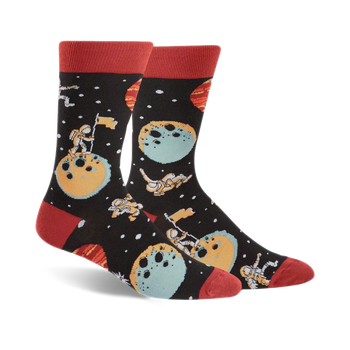 black-colored crew socks, featuring cartoon astronauts, moons, planets, stars in space design, with red toe and heel.   