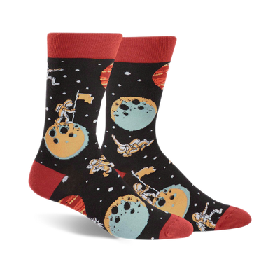 black-colored crew socks, featuring cartoon astronauts, moons, planets, stars in space design, with red toe and heel.   