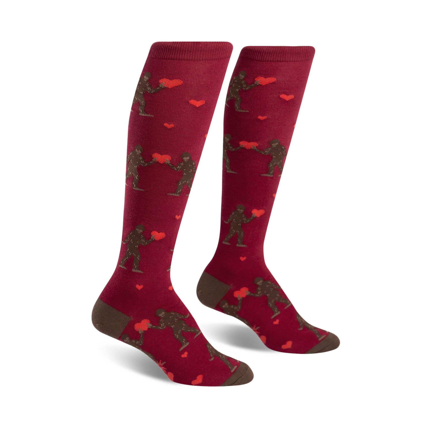 Pair of maroon knee-high socks. Features brown Bigfoot figures exchanging red hearts. Cute and quirky Valentine's Day design.