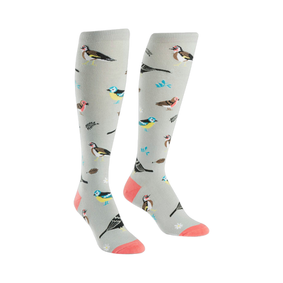 A pair of women's knee-high socks in light gray with a pattern of colorful birds and leaves. Coral-colored heel and toe.
