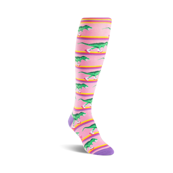 pink knee-high socks with graphic of green dinosaurs wearing purple roller skates on a yellow striped background.    }}