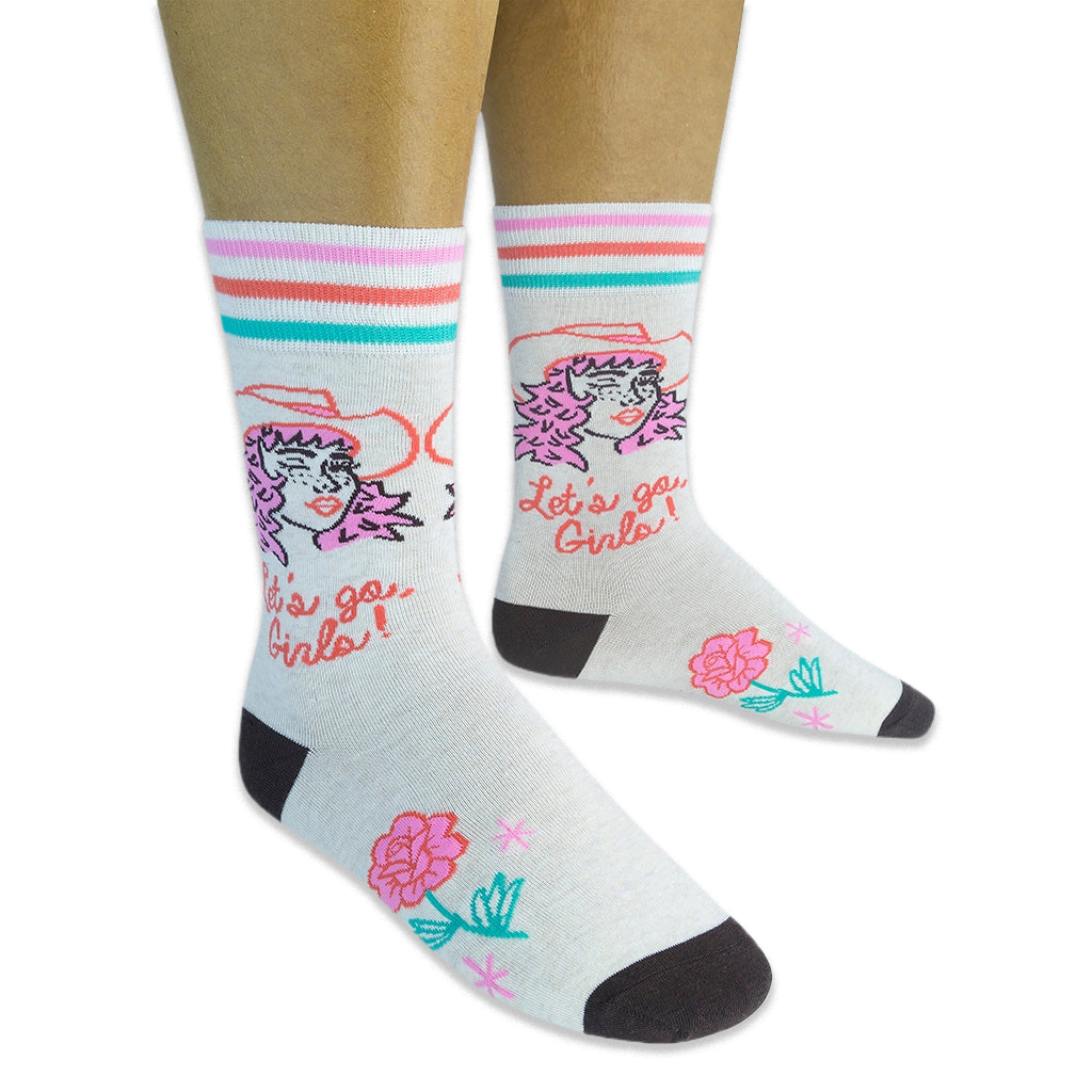 Person wearing cream socks with a pink-haired cowgirl, Let's go Girls text, retro stripes, and a pink rose on a black backdrop.