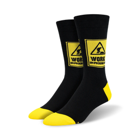 black crew socks with yellow accents display a bold "work in progress" warning sign pattern.   