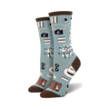A pair of crew socks in teal and mint green, featuring cameras, books, hats, and suitcases; the phrase 'Bon Voyage' is printed on the socks.