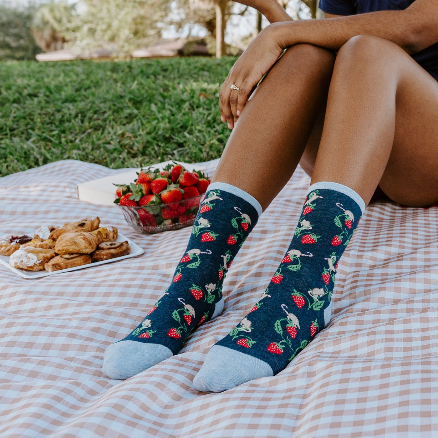 Lifestyle shot: Person wearing Berry Mice socks while enjoying a picnic outdoors. [lf]