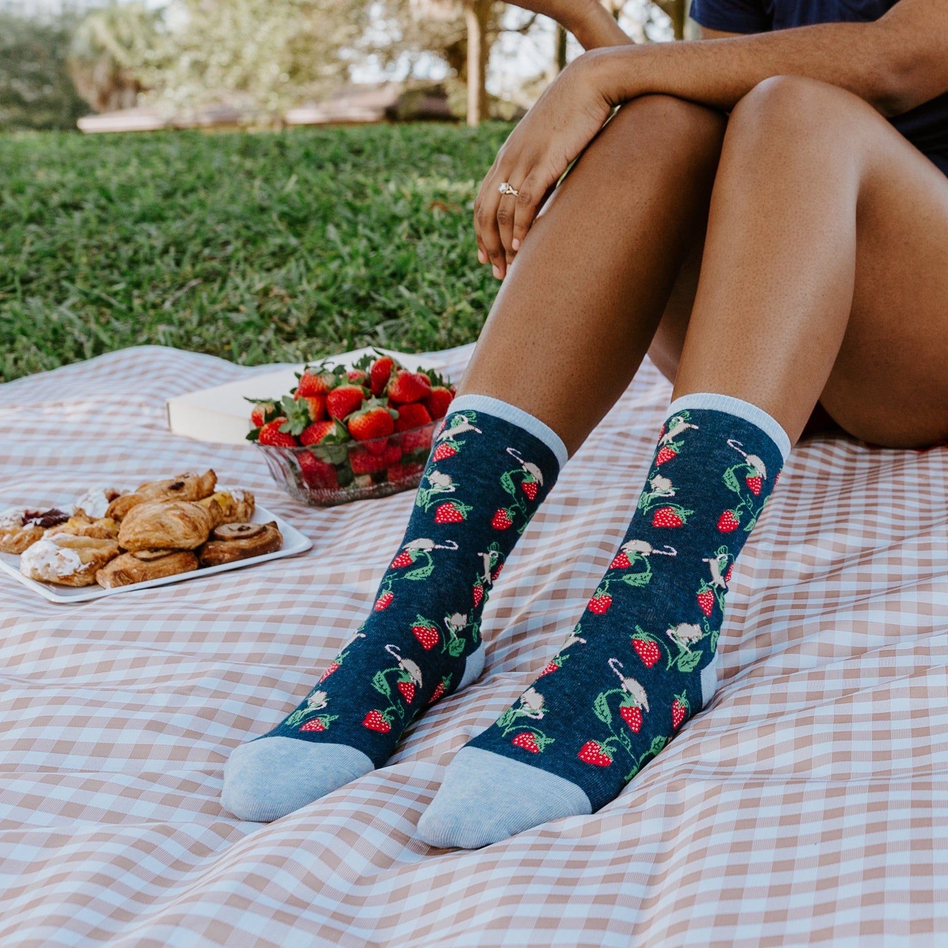 Lifestyle shot: Person wearing Berry Mice socks while enjoying a picnic outdoors. [lf]
