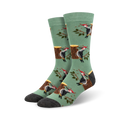 A pair of crew socks in sage green with a repeating pattern of woodpeckers on tree stumps and branches.