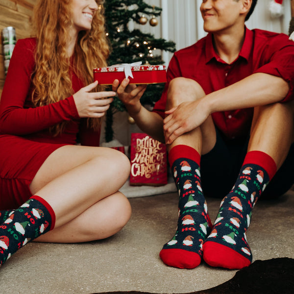 Lifestyle photo: Couple in Christmas attire sitting by a tree, showcasing the socks. [lf]