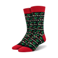 Pair of crew socks in black with a red cuff. The socks have a pattern of 'Merry Christmas' text and holly sprigs in green and red.