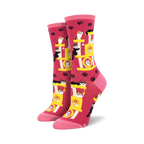 Crew socks in pink featuring a repeating pattern of cats playing on a yellow cat tree. Pink paw prints are scattered across the background.