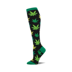 A single knee-high sock with a black background and a pattern of green and yellow marijuana leaves. The cuff is green.