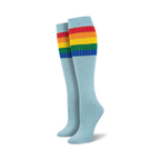Pair of light blue knee-high socks with a vibrant rainbow striped cuff against a white background.
