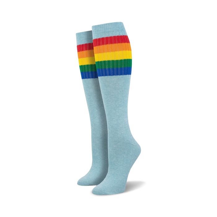 Pair of light blue knee-high socks with a vibrant rainbow striped cuff against a white background.