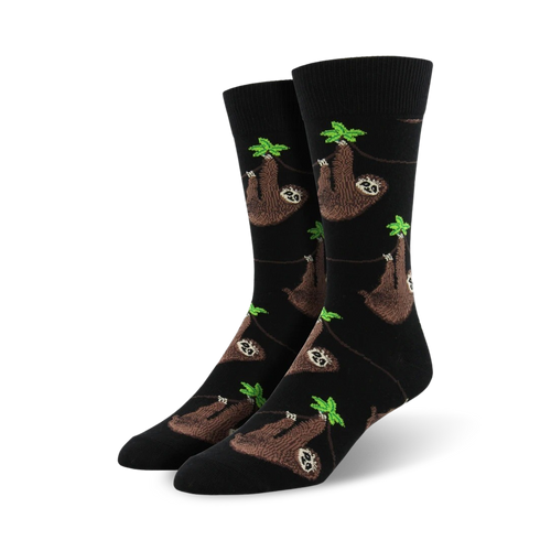 A pair of black crew socks with a repeating pattern of brown sloths hanging from green leaves. 