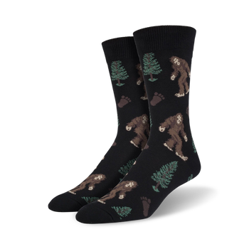 mens black crew socks with brown bigfoot creatures, green pine trees, and brown footprints  