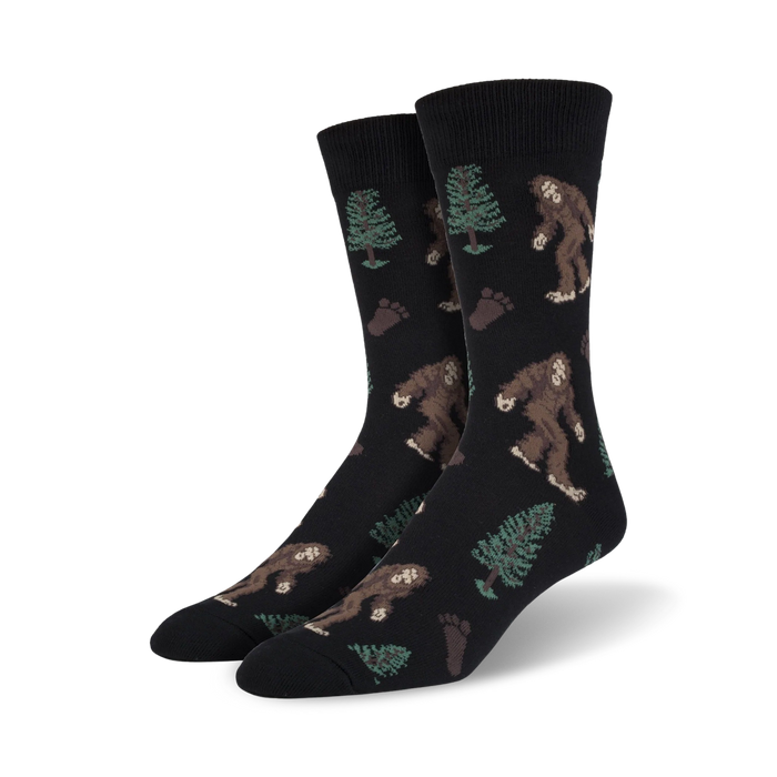mens black crew socks with brown bigfoot creatures, green pine trees, and brown footprints  